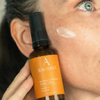 Applying Aureterra Botanical Peptide Cream to the cheek to hydrate, firm skin, and soften fine lines.